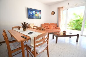 A living room with a wooden dining table, orange sofa, and a TV mounted on the wall.