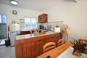 A kitchen with a central island, wooden cabinets, a refrigerator, a microwave, and a dining table with chairs.