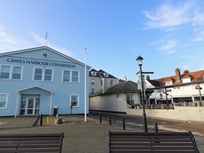 Een blauw gebouw met de tekst 'Cowes Harbour Commission', met een lantaarnpaal en banken ervoor.