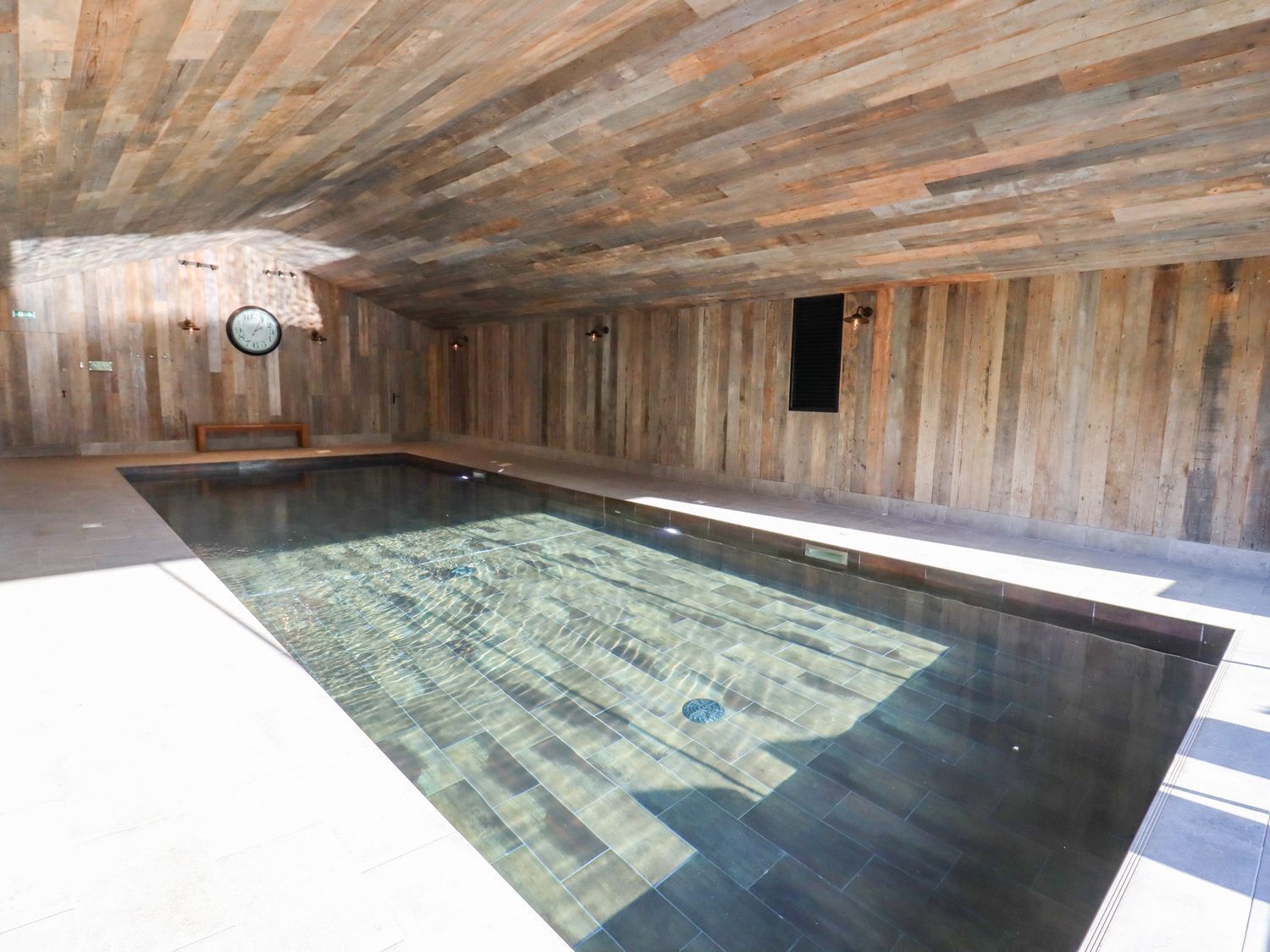 A large indoor swimming pool with wooden walls and a tiled floor.