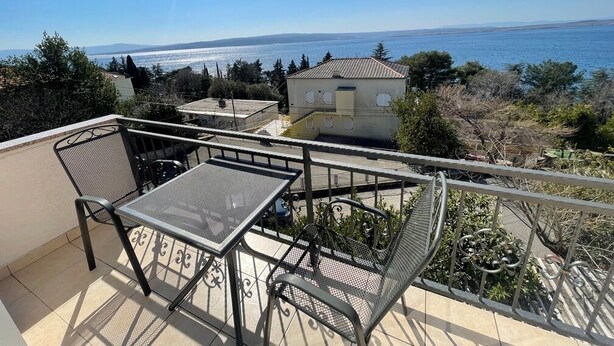 A balcony with a table and chairs, overlooking a body of water and distant land. - Apartman Kira 4 (Dramalj)