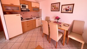 A compact kitchen with wooden cabinets, a microwave, and a dining area with a table and chairs. - Apartman Kira 4 (Dramalj)