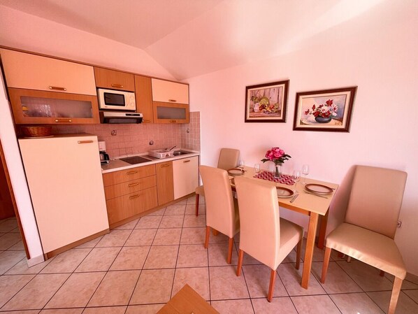 A compact kitchen with wooden cabinets, a microwave, and a dining area with a table and chairs. - Apartman Kira 4 (Dramalj)