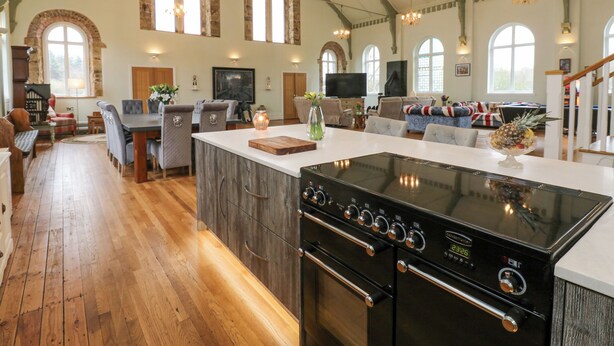A spacious kitchen with a central island, a dining area with a table and chairs, and a living room with sofas and a fireplace. - The Miners Hall Retreat (Stanley)