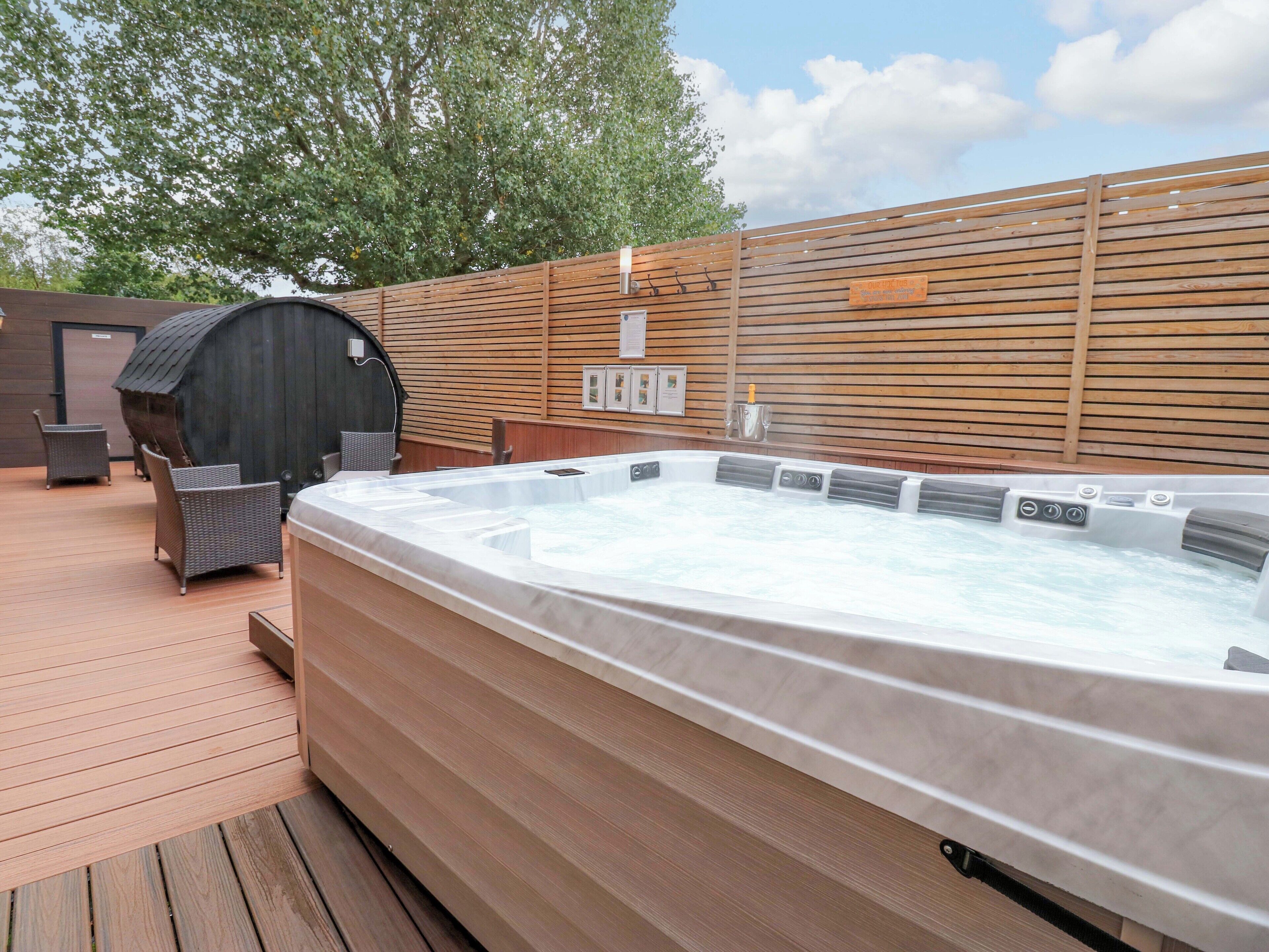A hot tub on a wooden deck with wicker chairs and a barbecue grill in the background.