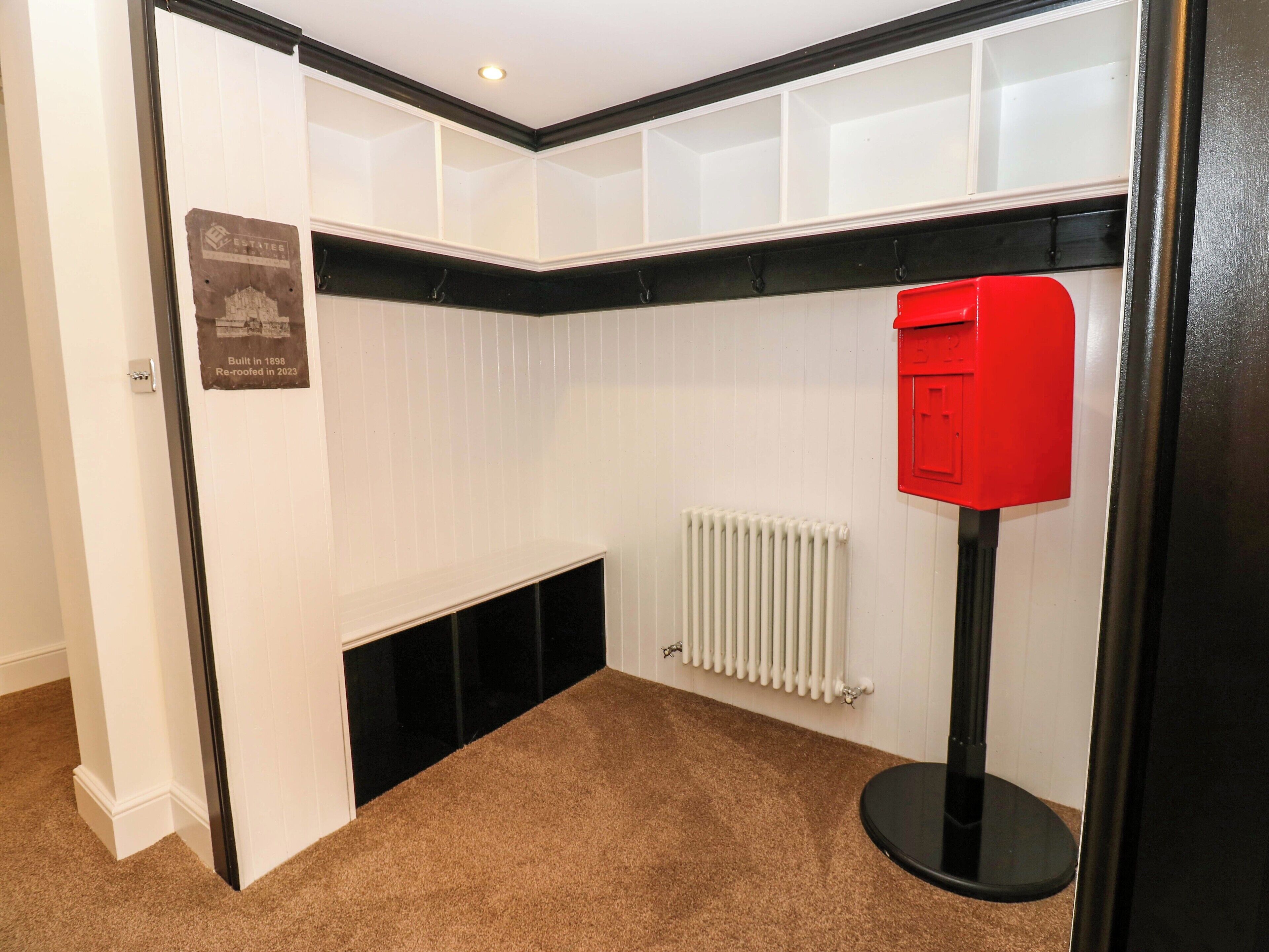 A corner room with a white radiator, a red mailbox, and a black shelf.