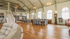 A spacious living area with a high ceiling, wooden flooring, and a dining area with a large table and chairs. - The Miners Hall Retreat (Stanley)