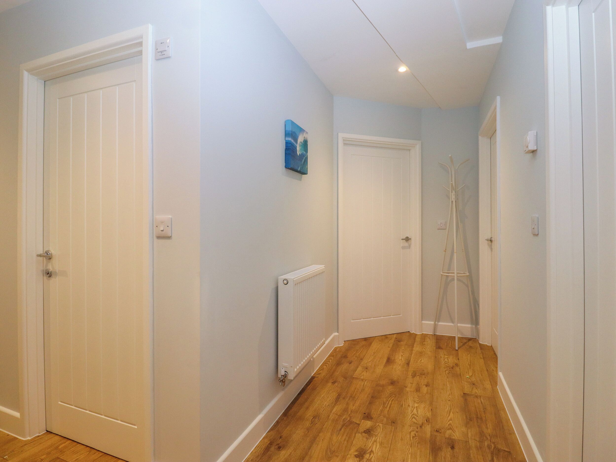 A hallway with wooden flooring, white doors, and a radiator.