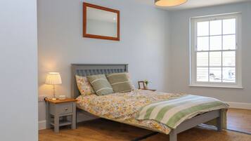 A bedroom with a bed, a nightstand, a lamp, a mirror, and a window.