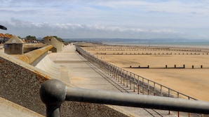 A coastal promenade with a concrete barrier and a metal railing. - The Seven Sands (Romney Marsh)