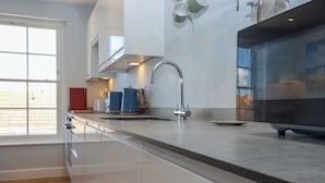 A modern kitchen with a stainless steel sink, a coffee maker, and a window providing natural light. - The Seven Sands (Romney Marsh)