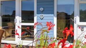 A cottage with a blue exterior, a white door, and a glass door leading to a patio area. - Cape A1 (Yarmouth)