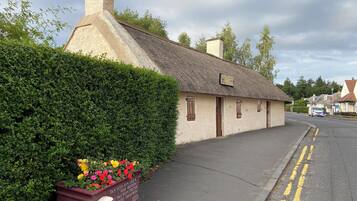 Une maison de campagne traditionnelle à toit de chaume, avec une enseigne indiquant qu’il s’agit d’une maison d’hôtes.