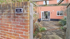 Un muro in mattoni con un cartello con il numero civico, un cancello in legno e un vialetto lastricato che conduce a una casa con tetto in tegole.