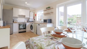 Cucina compatta con lavatrice, forno e microonde. C'è una zona pranzo con tavolo apparecchiato per quattro, e una finestra con vista all'esterno.