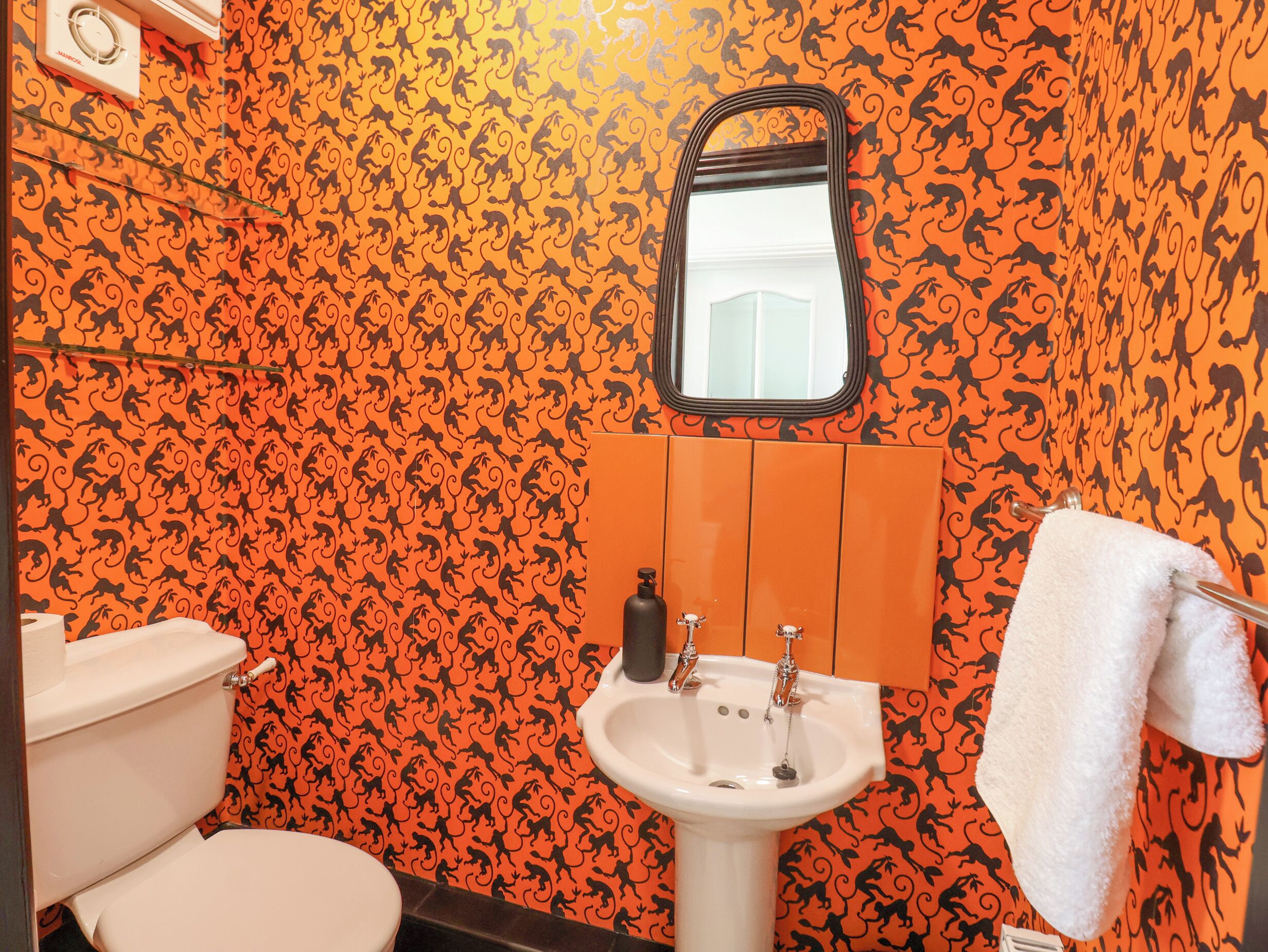 A bathroom with a toilet, sink, and mirror. The walls are covered with a monkey pattern wallpaper.