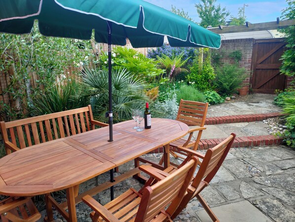 A wooden table with chairs and a green umbrella in a garden setting. - 23 Church Farm Lane (Halesworth)