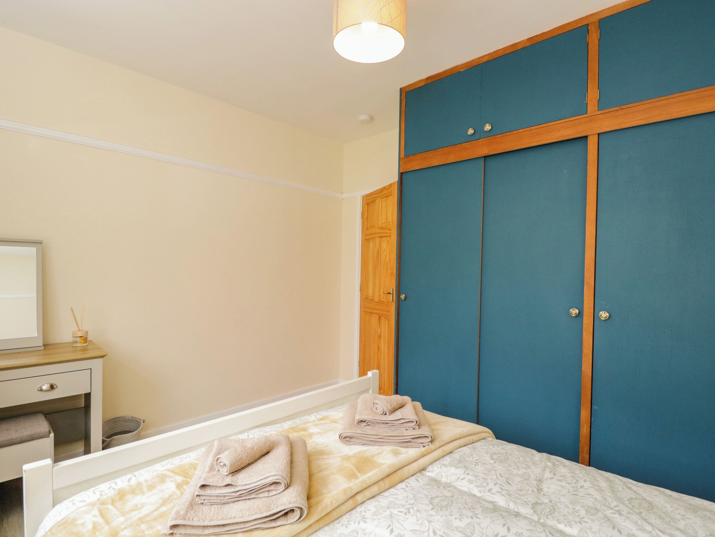 A bedroom with a bed, a bedside table, a desk, and a wardrobe.
