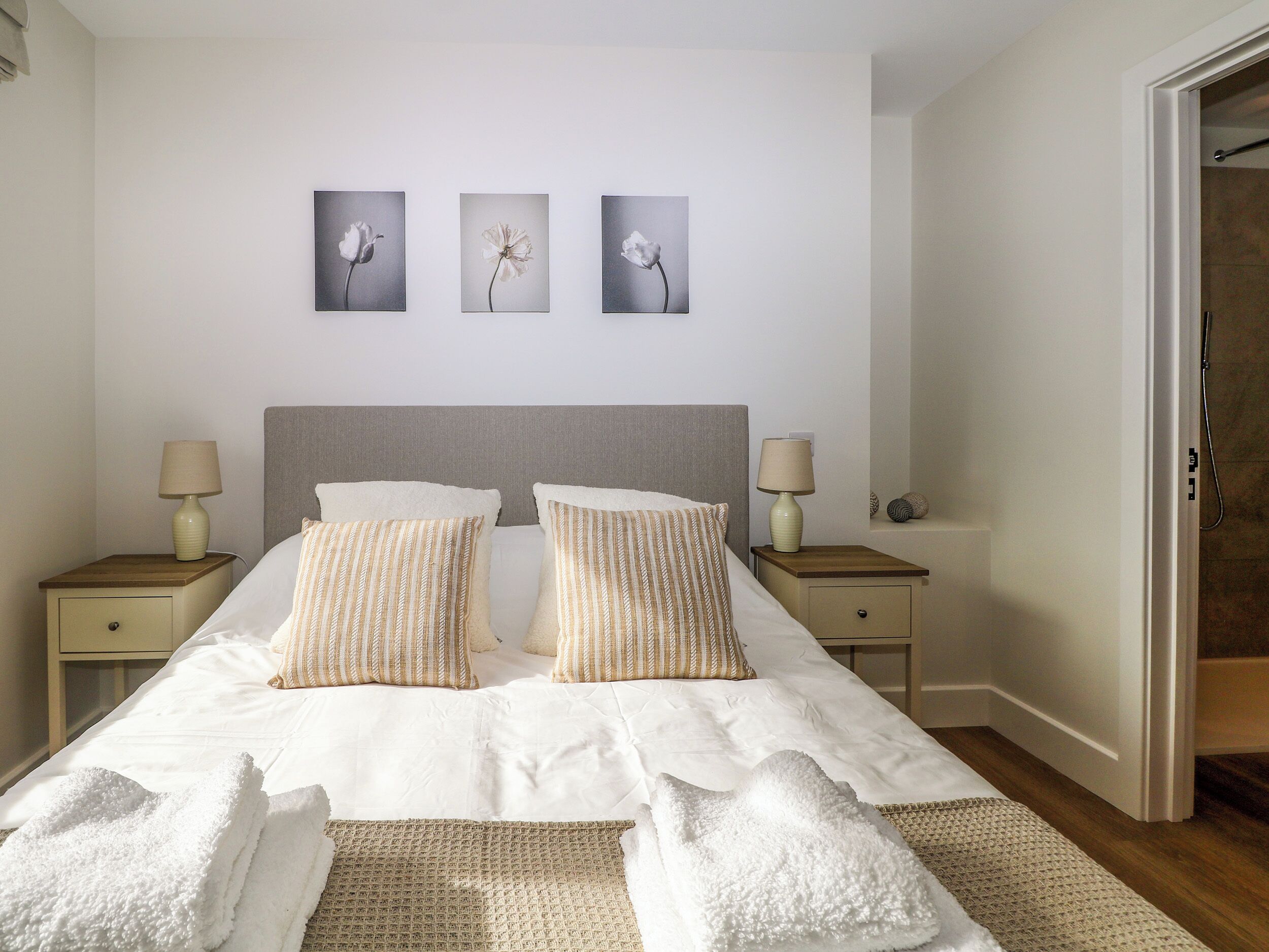 A neatly made bed with two pillows, a bedside table with a lamp, and three framed pictures on the wall.