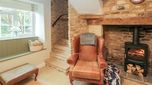A cozy room with a stone fireplace, a wooden bench, and a chair with a blanket. - Thorn Cottage (Fairford)