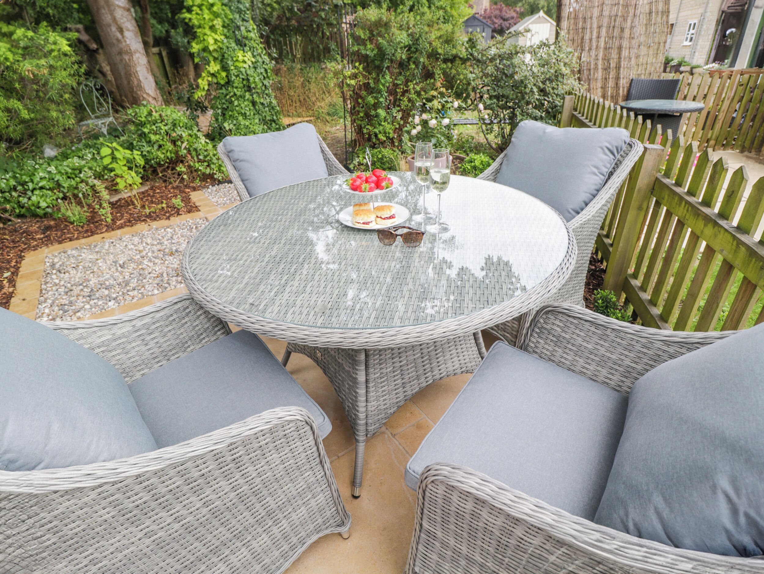 A round glass table with wicker chairs, a plate of food, and wine glasses.