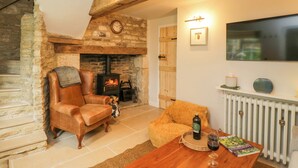 A cozy living room with a stone fireplace, leather armchair, and a wooden coffee table. - Thorn Cottage (Fairford)
