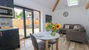 Een moderne keuken met een inbouwoven en magnetron, een eethoek met tafel en stoelen, een bank en een groot raam met uitzicht op de achtertuin.