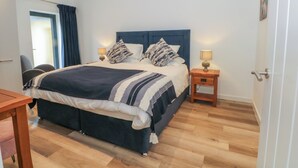 Een moderne slaapkamer met een groot bed, twee nachtkastjes met lampen, een houten bureau en een stoel.