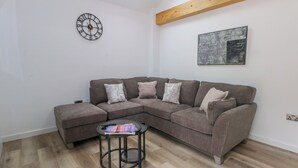 Een woonkamer met een modulaire bank, een ronde salontafel, een wandklok en een schilderij.