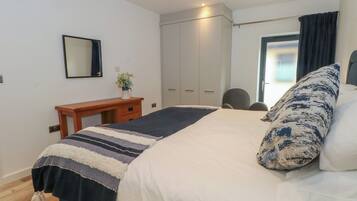 A bedroom with a bed, a desk, a wardrobe, and a window with curtains.