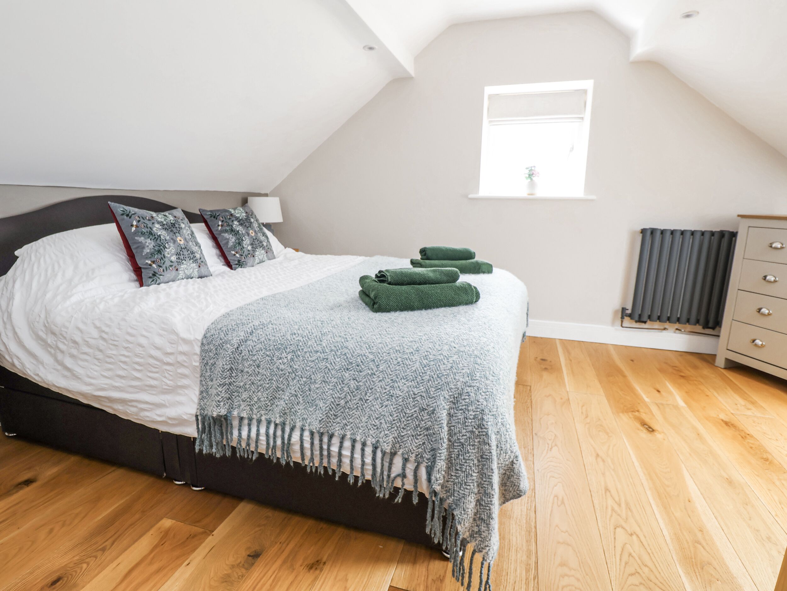 A bedroom with a bed, pillows, a blanket, and a radiator.