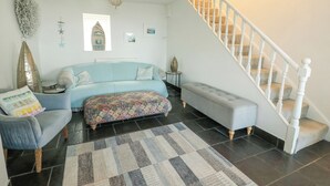 Una sala de estar con un sofá azul, un reposapiés estampado, una alfombra, una escalera blanca y una araña.
