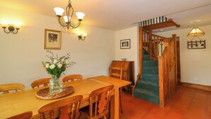 A dining area with a wooden table and chairs, a vase of flowers, wall-mounted lights, and a staircase with a wooden railing. - Canny Croft (Bridgwater)