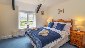 A bedroom with a large bed, two bedside tables with lamps, a window with a view, and a radiator. - Canny Croft (Bridgwater)