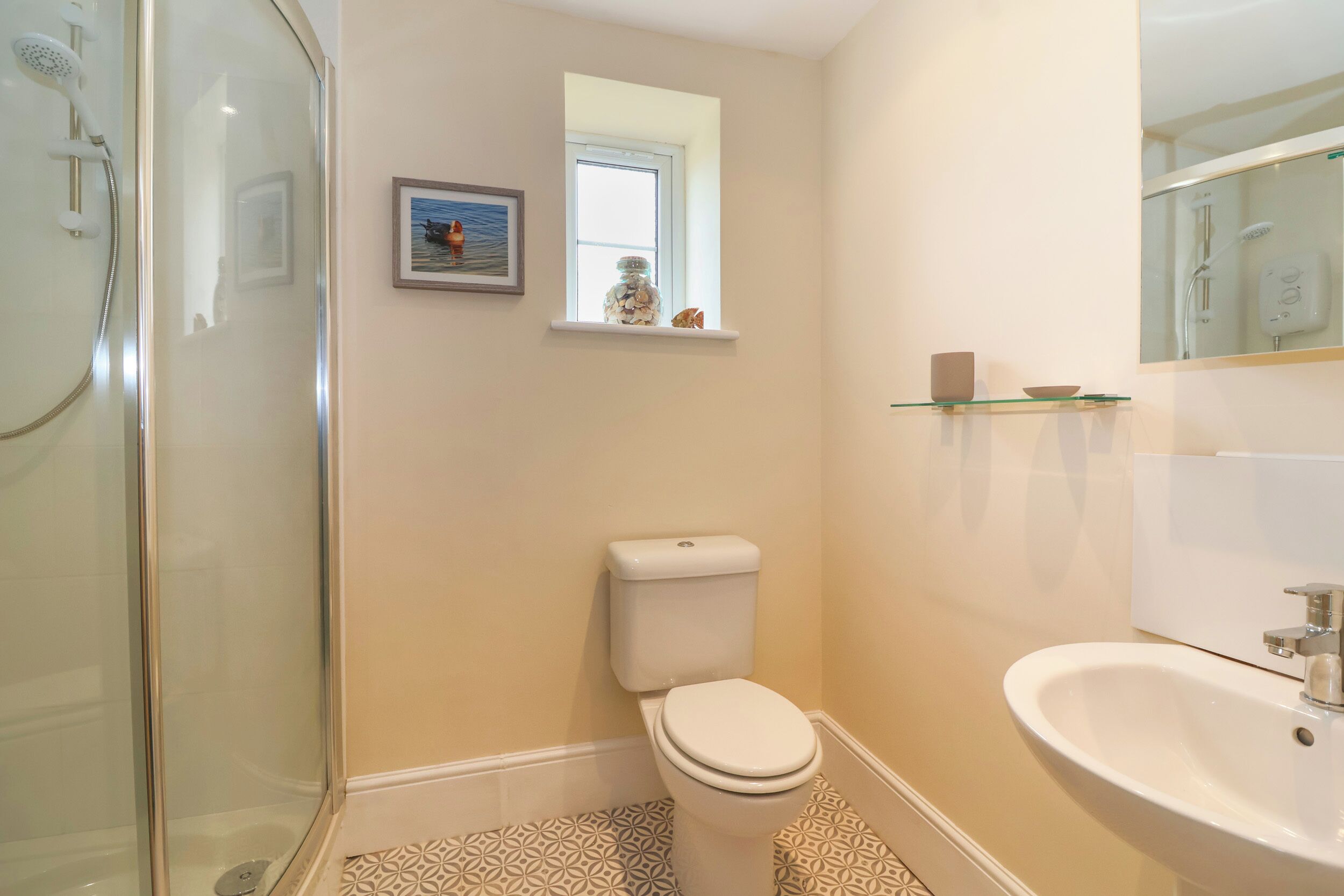 Une salle de bain avec une douche à parois de verre, des toilettes, un lavabo et une petite fenêtre avec un tableau.