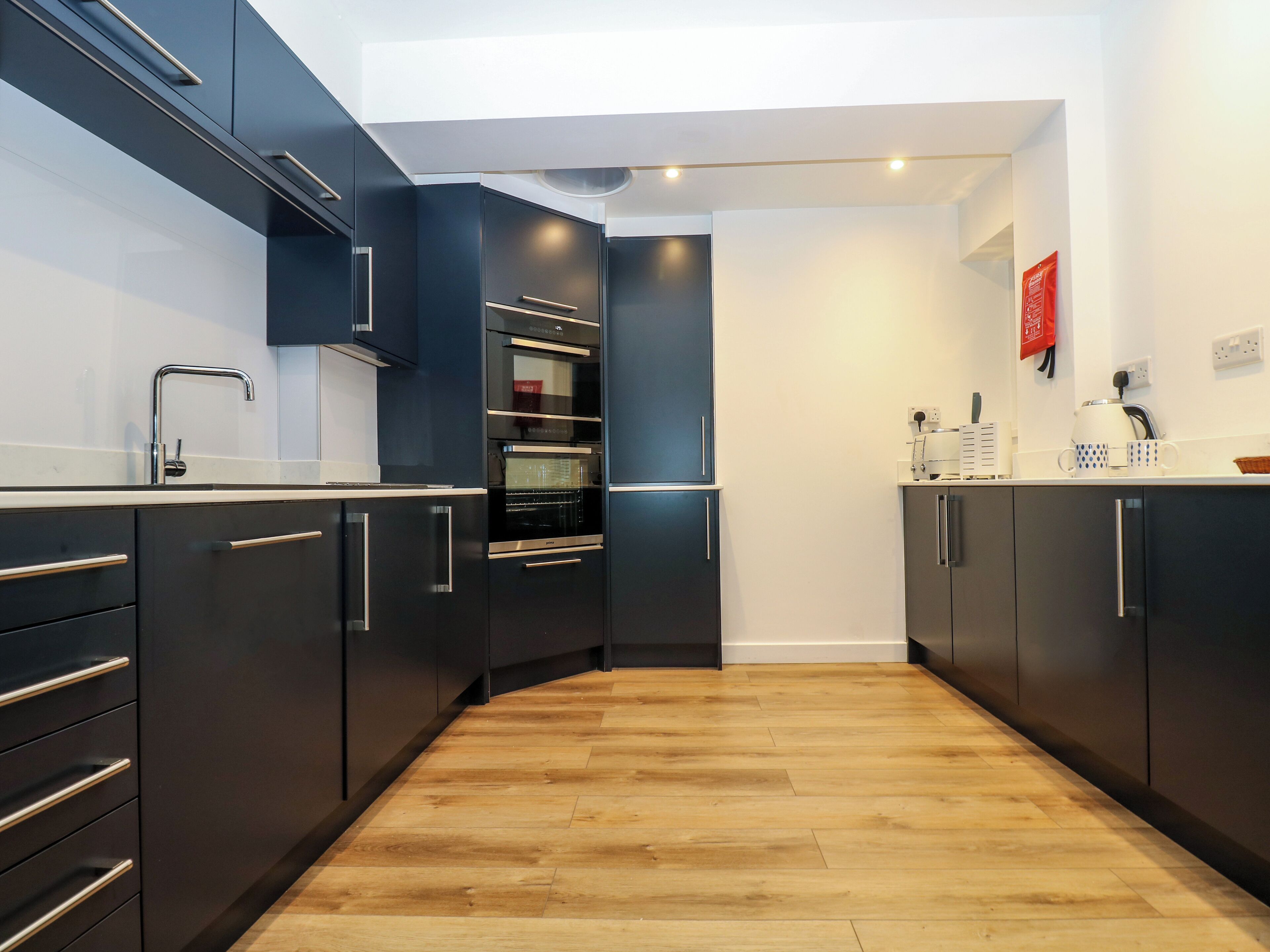 Une cuisine moderne avec des meubles de couleur sombre, une hotte en acier inoxydable et un plancher en bois.