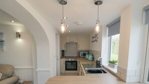 Een moderne keuken met een centraal eiland, roestvrijstalen apparatuur en hangende verlichting.