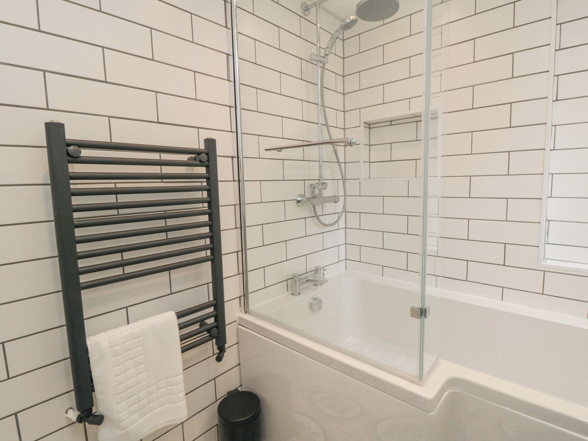 A modern bathroom with a glass-enclosed shower, a white bathtub, and a black towel rack with a white towel.