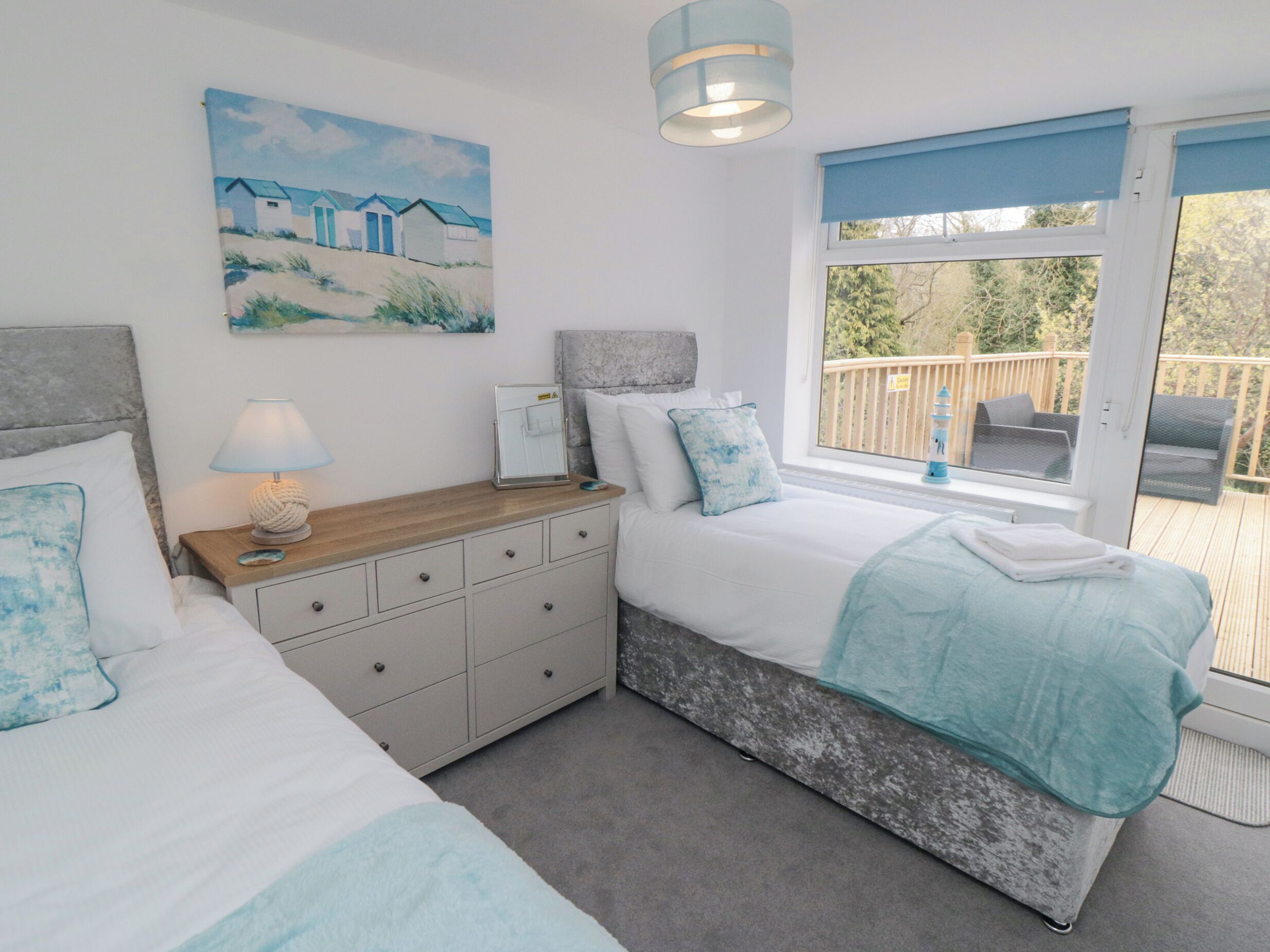 A bedroom with a bed, a nightstand, a dresser, a window with a view of a deck, and a painting on the wall.