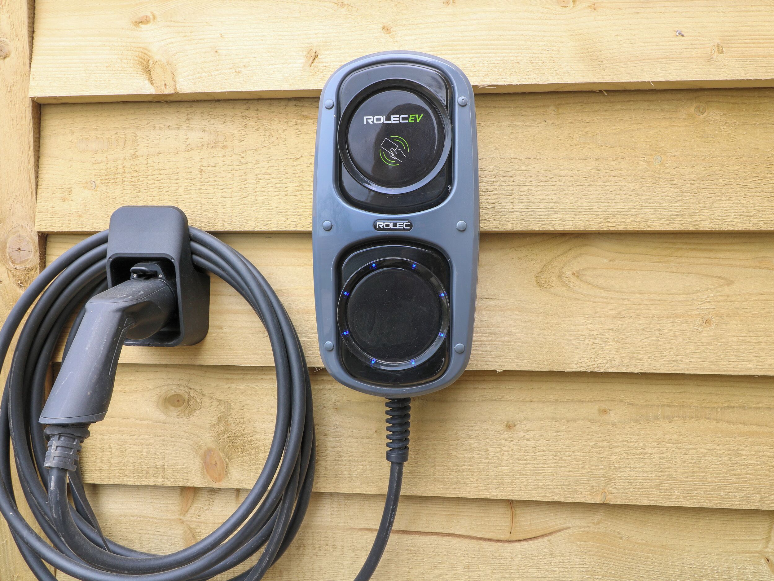 Una estación de carga ROLEC para vehículos eléctricos montada en una pared de madera.