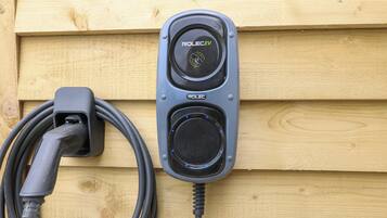 Una estación de carga ROLEC para vehículos eléctricos montada en una pared de madera.