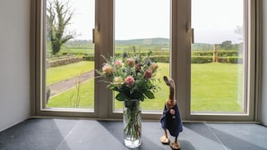 Et klart vue over et landligt landskab gennem et stort vindue, med en blomstervase på et vindueskarm.