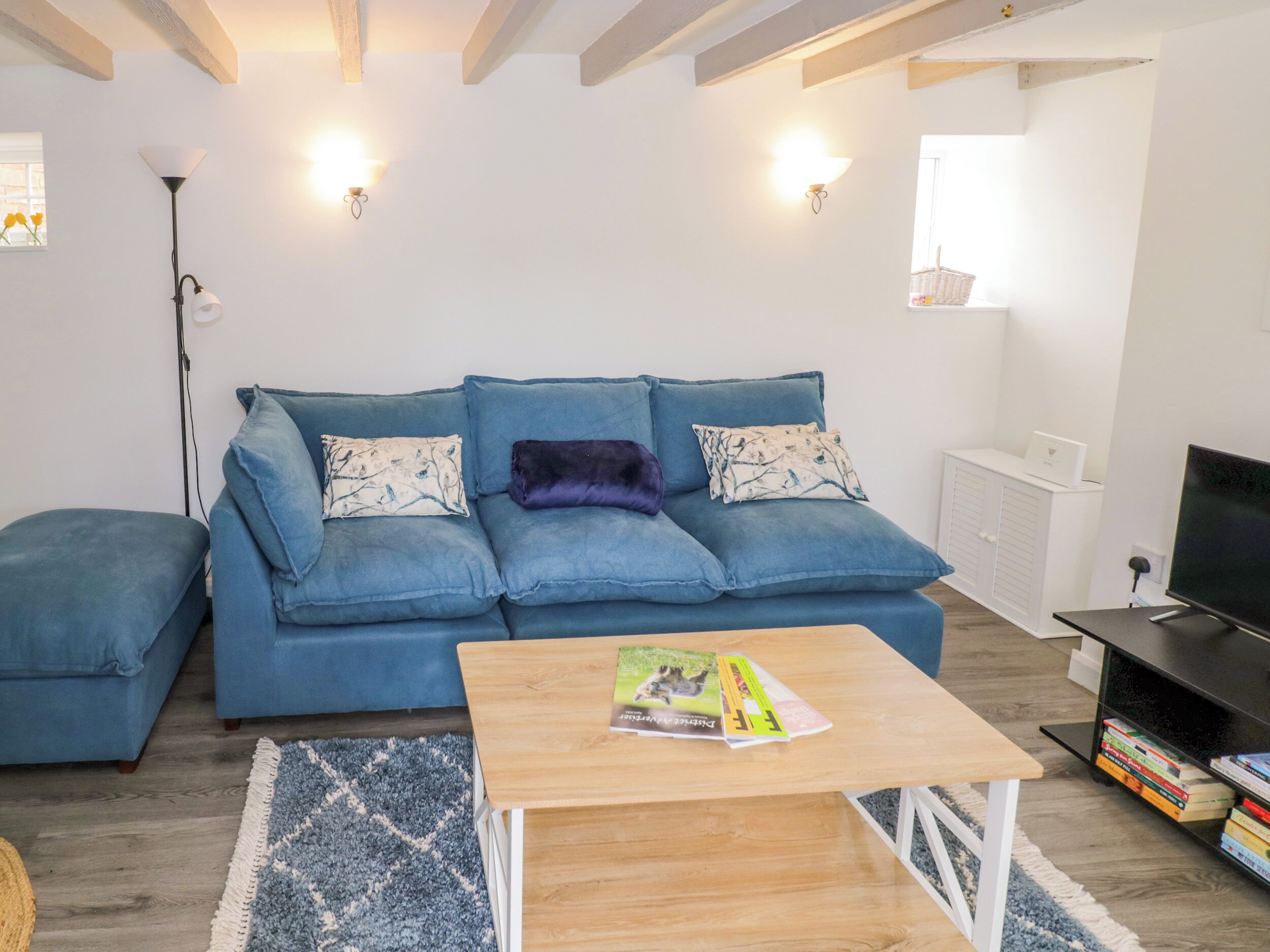 A living room with a blue sofa, a wooden coffee table, a TV stand with a TV, and a bookshelf.