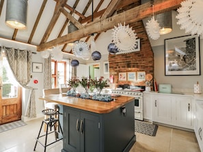 A kitchen with a central island, wooden beams, hanging paper lanterns, and a brick wall. - The Old Byre (Salisbury)
