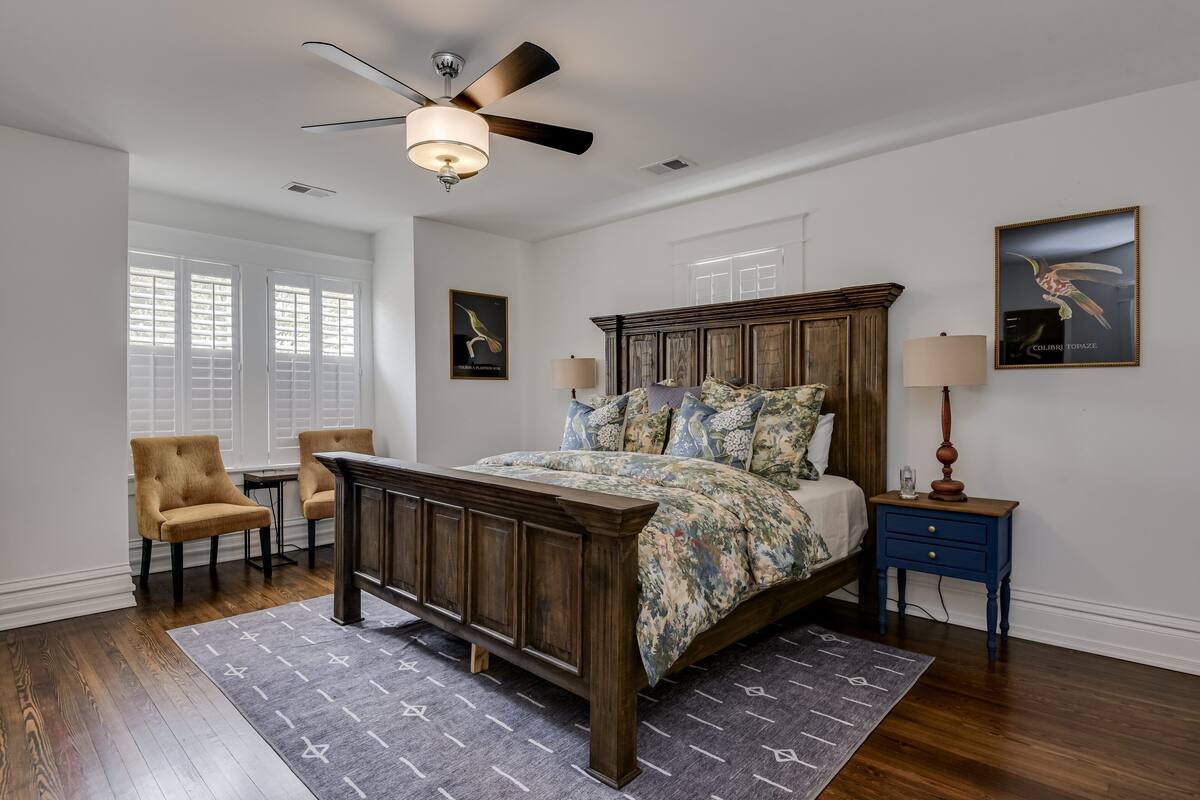 A bedroom with a wooden bed, a ceiling fan, a nightstand, a chair, and a window with blinds.