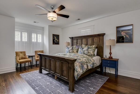 A bedroom with a wooden bed, a ceiling fan, a nightstand, a chair, and a window with blinds. - Burrell and Flynn's Farm (Aiken)