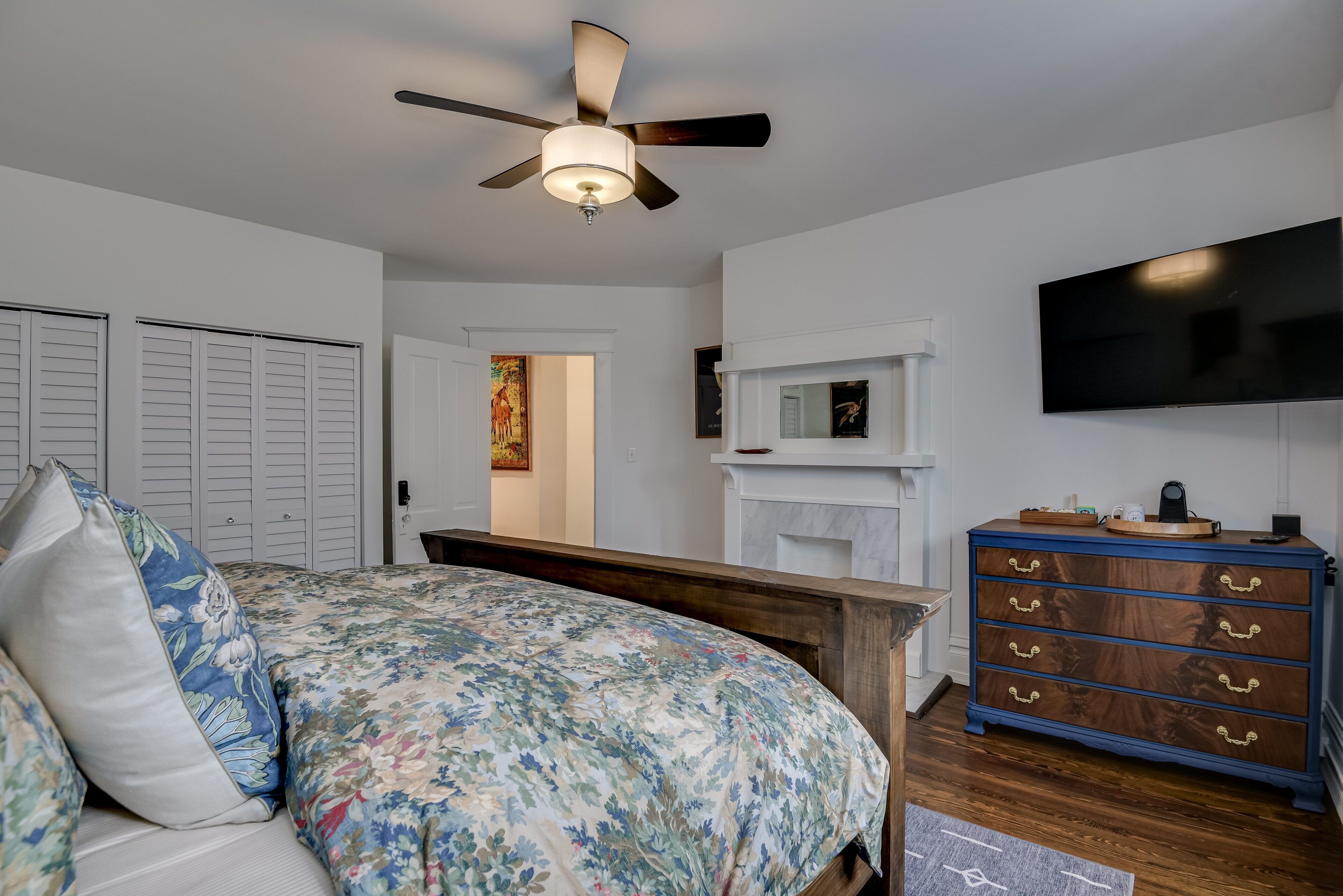 Une chambre à coucher avec un lit, une commode, un ventilateur de plafond, une télévision et une cheminée.