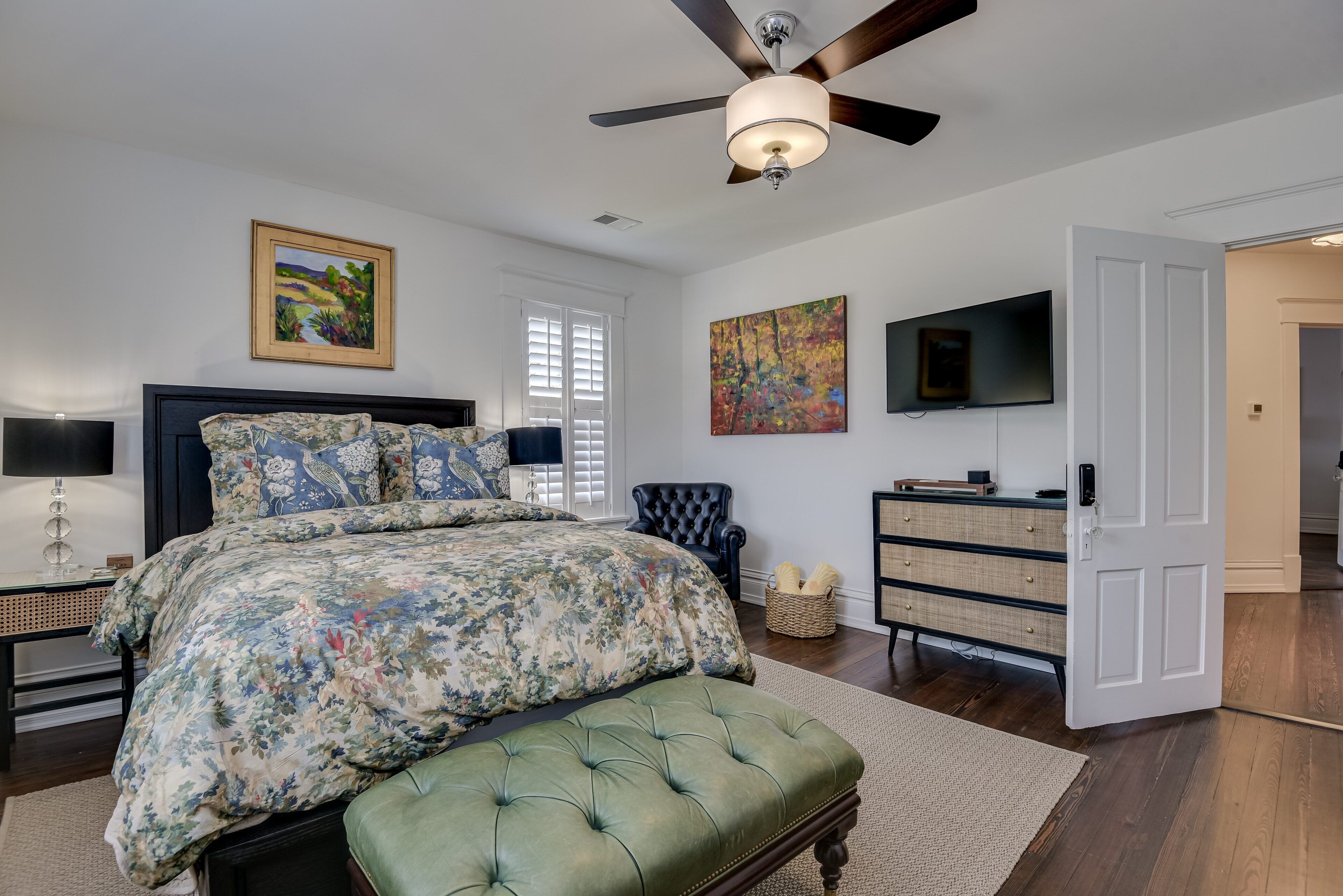 A bedroom with a large bed, a ceiling fan, a TV, and a dresser.