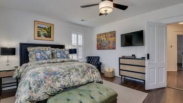 A bedroom with a large bed, a ceiling fan, a TV, and a dresser.