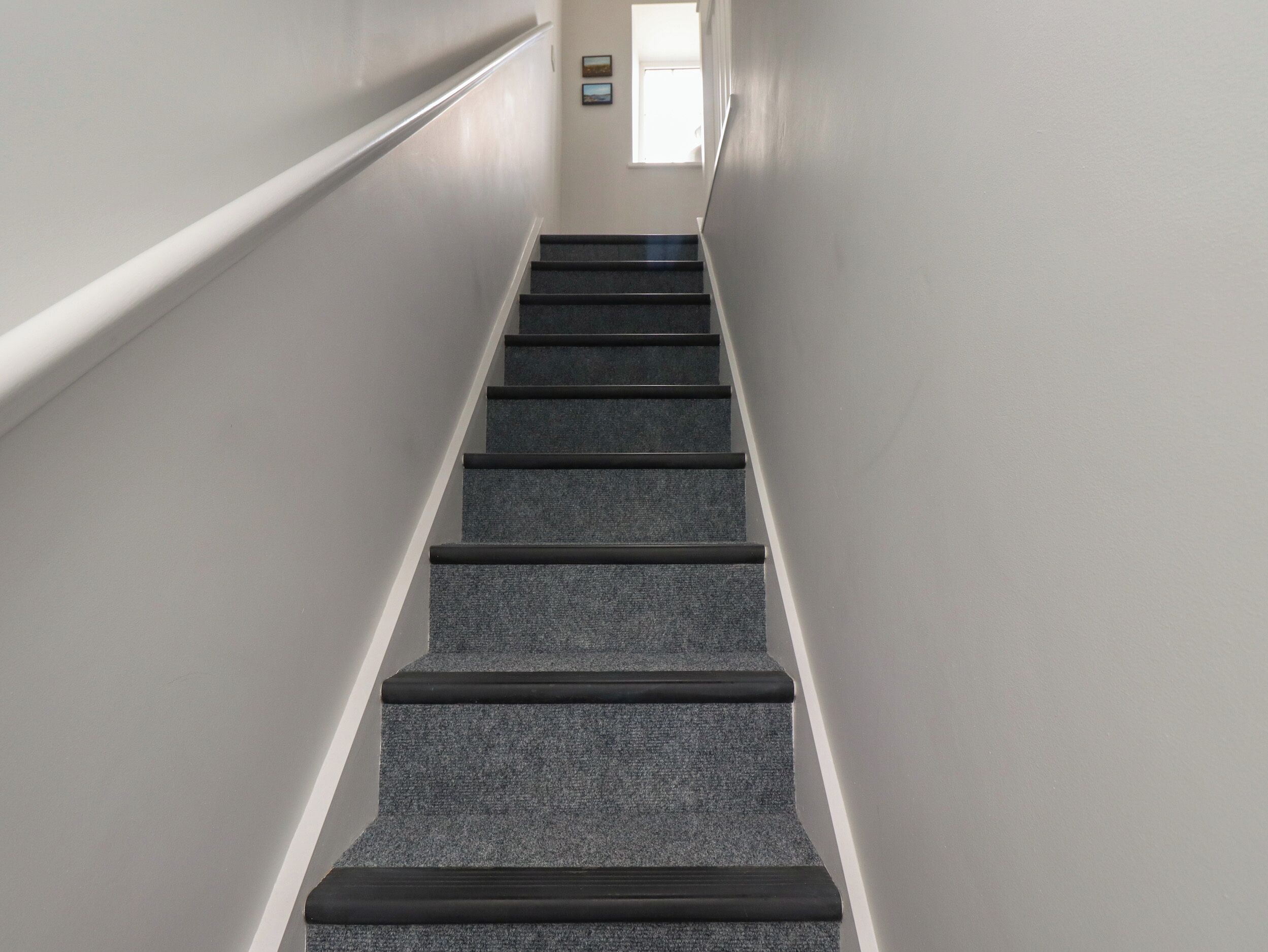Un escalier dont les marches sont recouvertes de moquette et les murs peints en blanc.